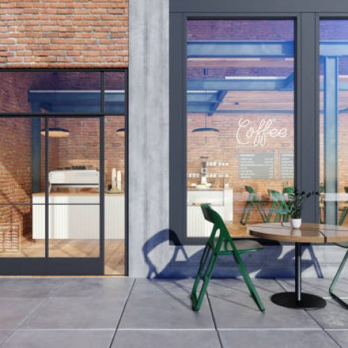 Store Window Of Coffee Shop With Table, Green Chairs In Front Of Shop And Brick Wall Background.